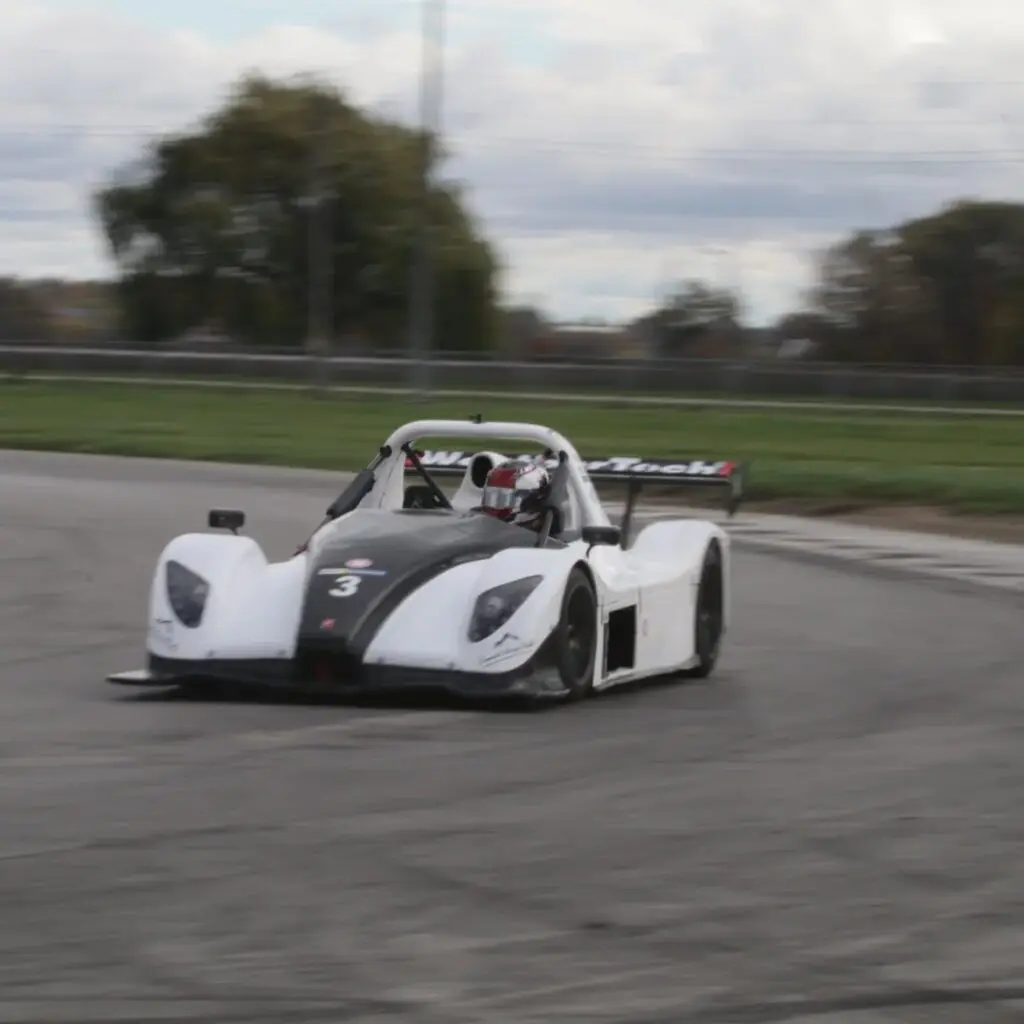 Open-cockpit race car with number 3, white and black livery, taking a turn on a racetrack with a driver in a red helmet.
