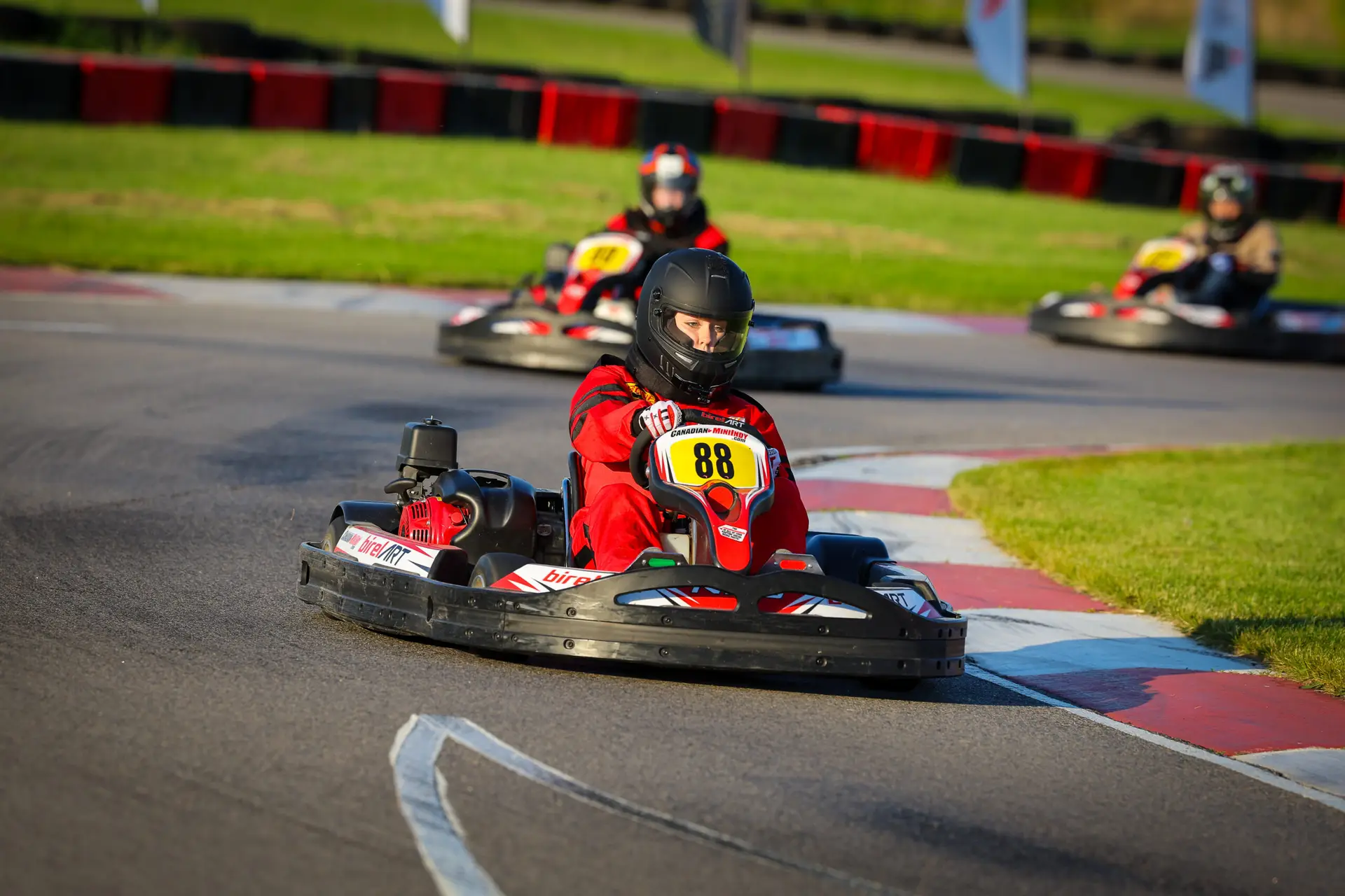 Karti racing scene with a driver in red suit wearing a black helmet, steering a go-kart marked number 88 on an outdoor track.